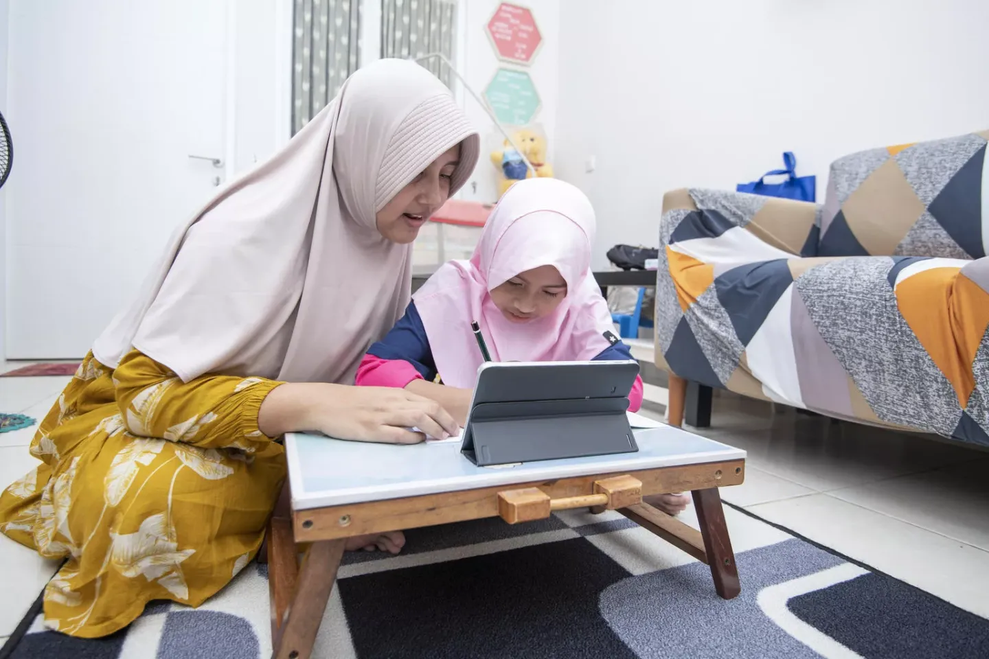A mother helps her daughter use a digital tablet.