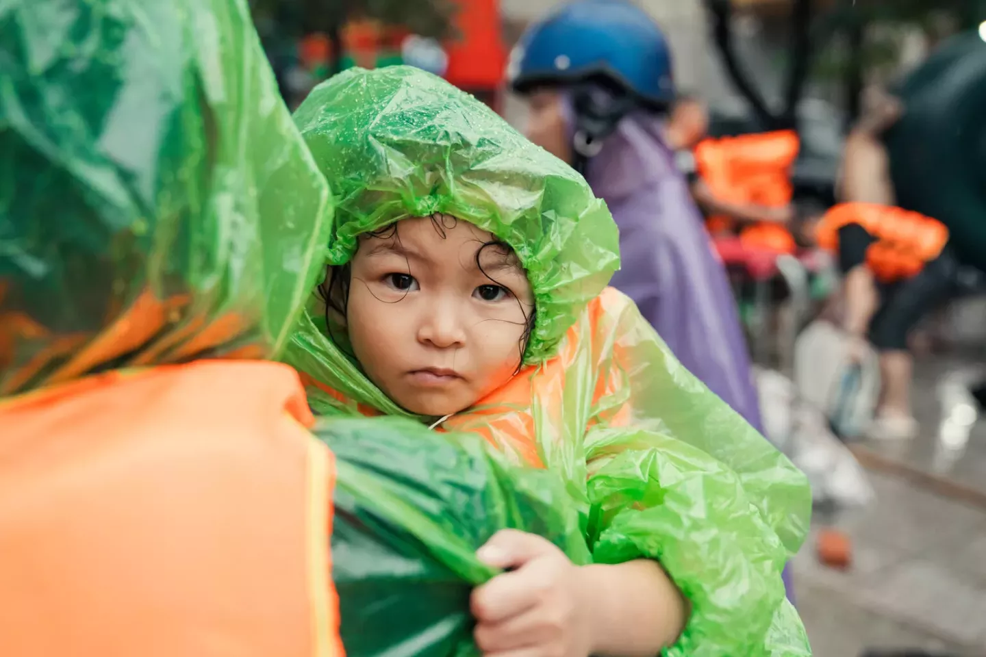 A mother holding a girl, both wearing raincoats and evacuating during a flood