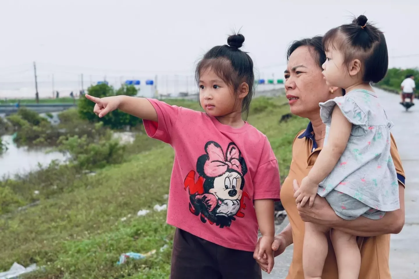 Do Ngoc Anh (in pink), her grandmother Tran Thi Noi, and younger sister Do Lan Anh stand on the sea dyke in Hai Tien commune, Ninh Binh province, ahead of Typhoon Wipha making landfall.
