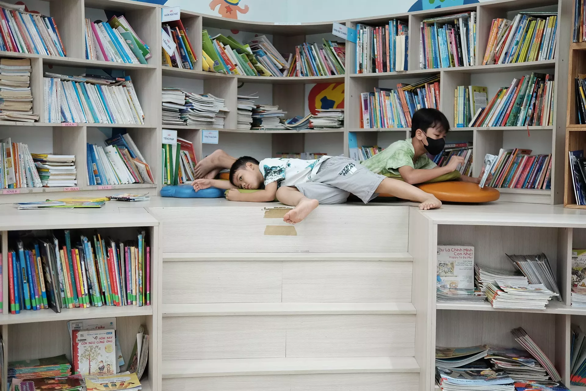 Two boys lying in opposite directions in a library.