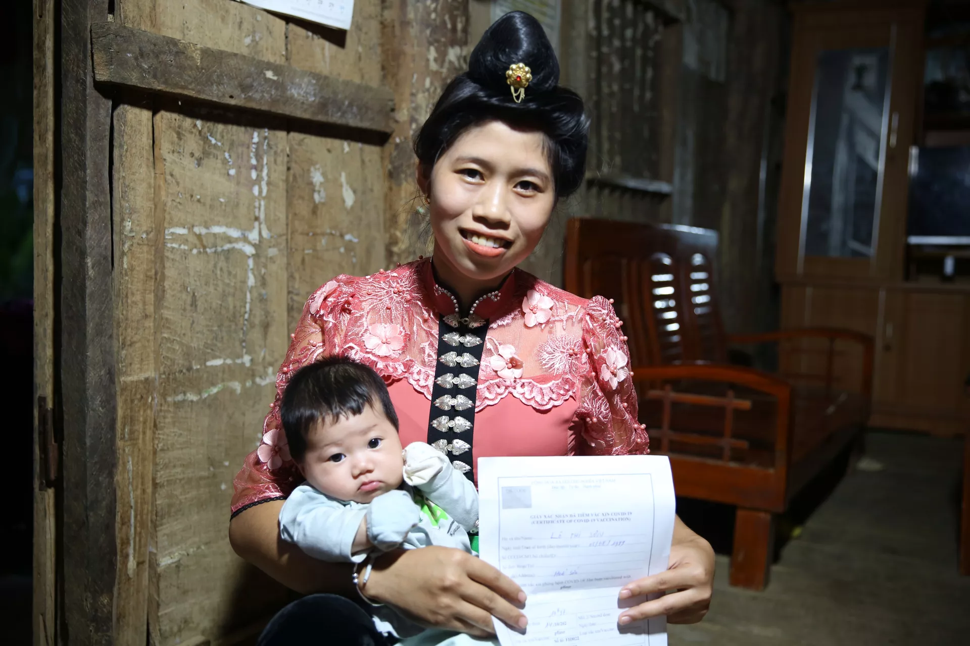 Lò Thị Sơn bế con gái và giấy chứng nhận tiêm vắc-xin COVID-19