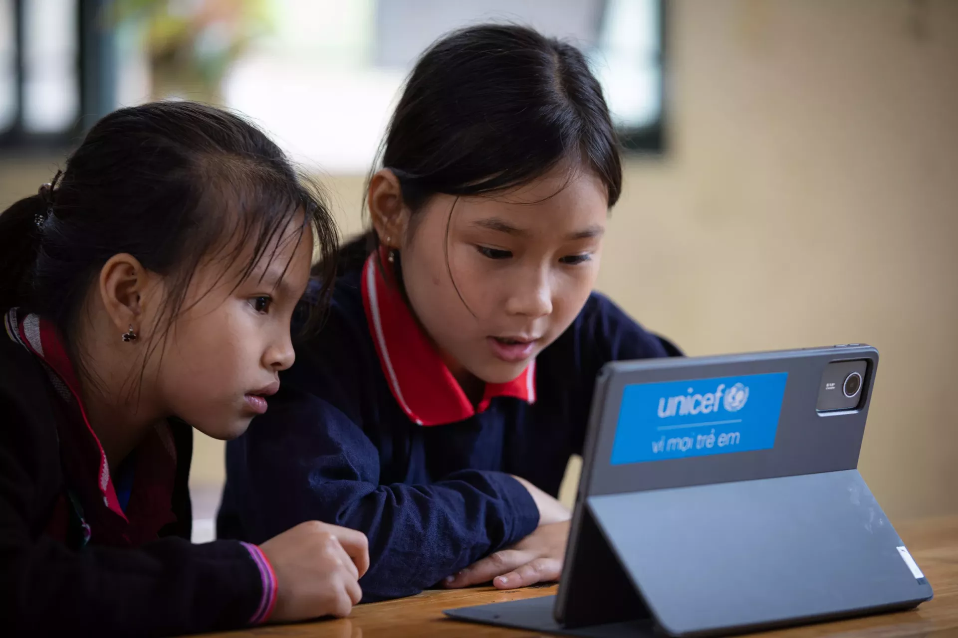 Hai b&eacute; g&aacute;i mỉm cười khi chơi với m&aacute;y t&iacute;nh bảng do UNICEF hỗ trợ.