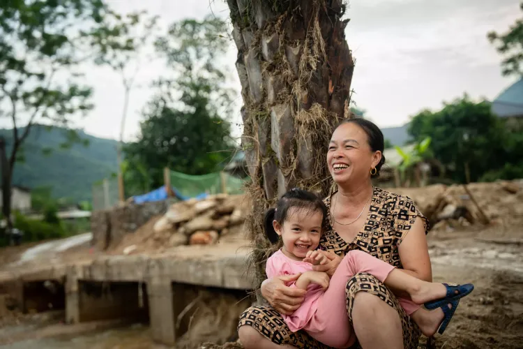 A girl and a grandma laughing. Besides them are the debris left by a flashflood and a landslide