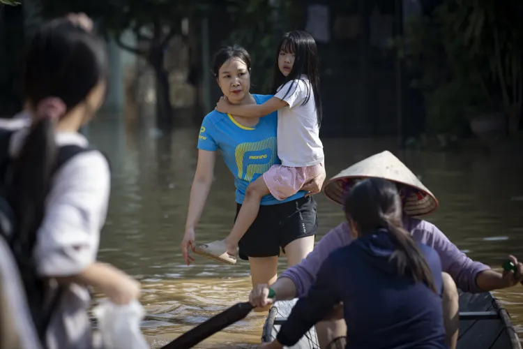 Người mẹ bế con qua con đường bị ngập do ảnh hưởng từ b&atilde;o 