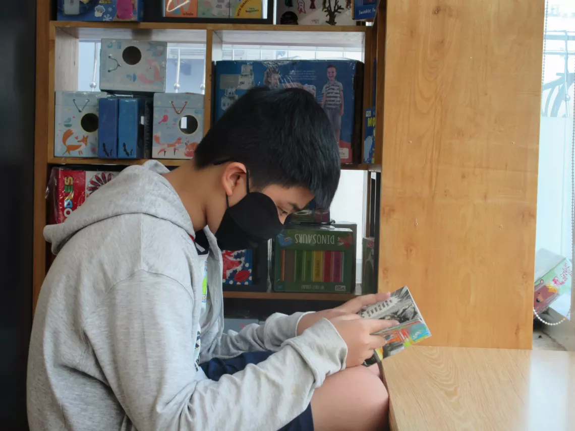 A boy with mask sitting and reading