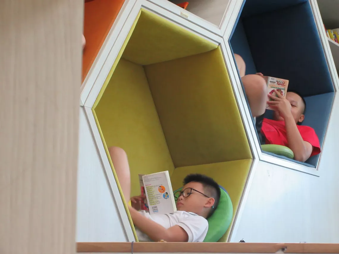 Two children, comfortably reading books, curl up in colorful small hexagons at the library.