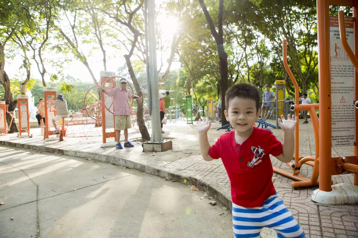 A boy smiles with both his arms up. He is standing near the road.