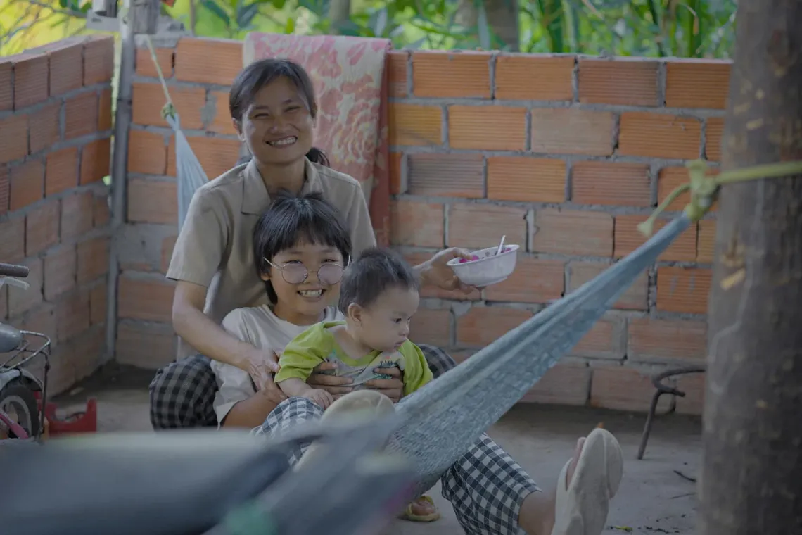 Loan sits with her children, 10-year-old Bi and 11-month-old Bối Bối, on a hammock at home in Dak Lak province.