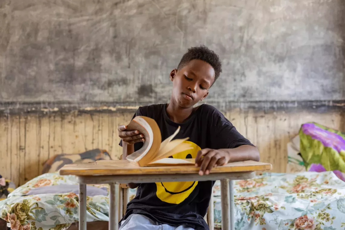 A boy in an empty classroom in Port Sudan flips through the pages of a book.