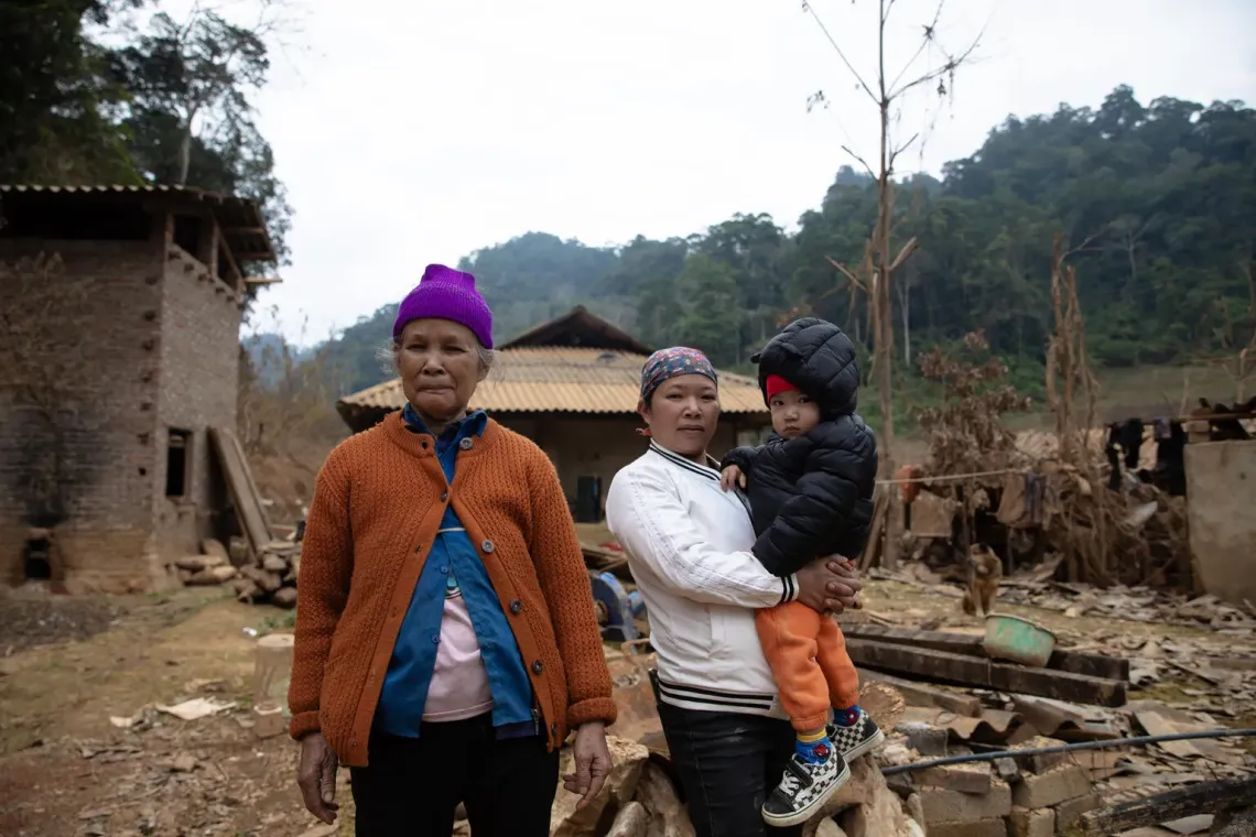 Từ tr&aacute;i sang phải: B&agrave; Ho&agrave;ng Thị Chẹ, chị B&agrave;n Thị Say v&agrave; b&eacute; M&atilde; Việt Cường đứng tại khoảng s&acirc;n sau nh&agrave; &ndash; nơi từng ch&igrave;m trong nước lũ suốt 25 ng&agrave;y li&ecirc;n tiếp trong c&aacute;c đợt b&atilde;o lũ trong năm 2025.