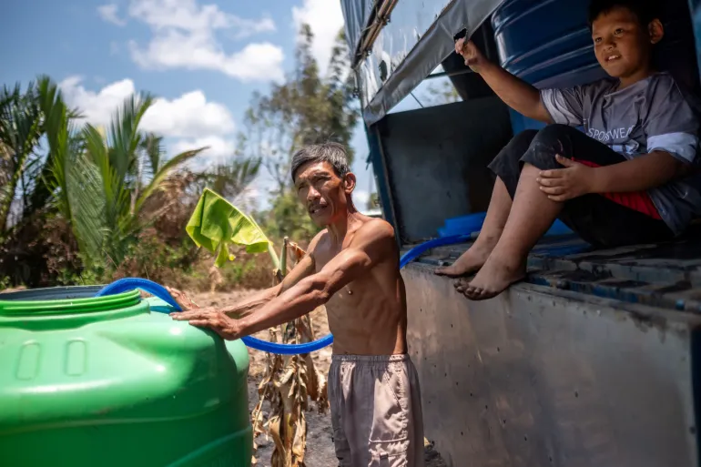 Vo Thanh Thuan and his son fill up their plastic tank with fresh water delivered by sponsors from nearby provinces in Tan Phu Dong District, Tien Giang Province, Vietnam, on Tuesday, April 23, 2024. 