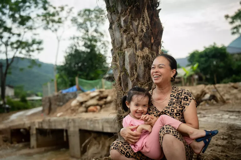 A girl and a grandma laughing. Besides them are the debris left by a flashflood and a landslide