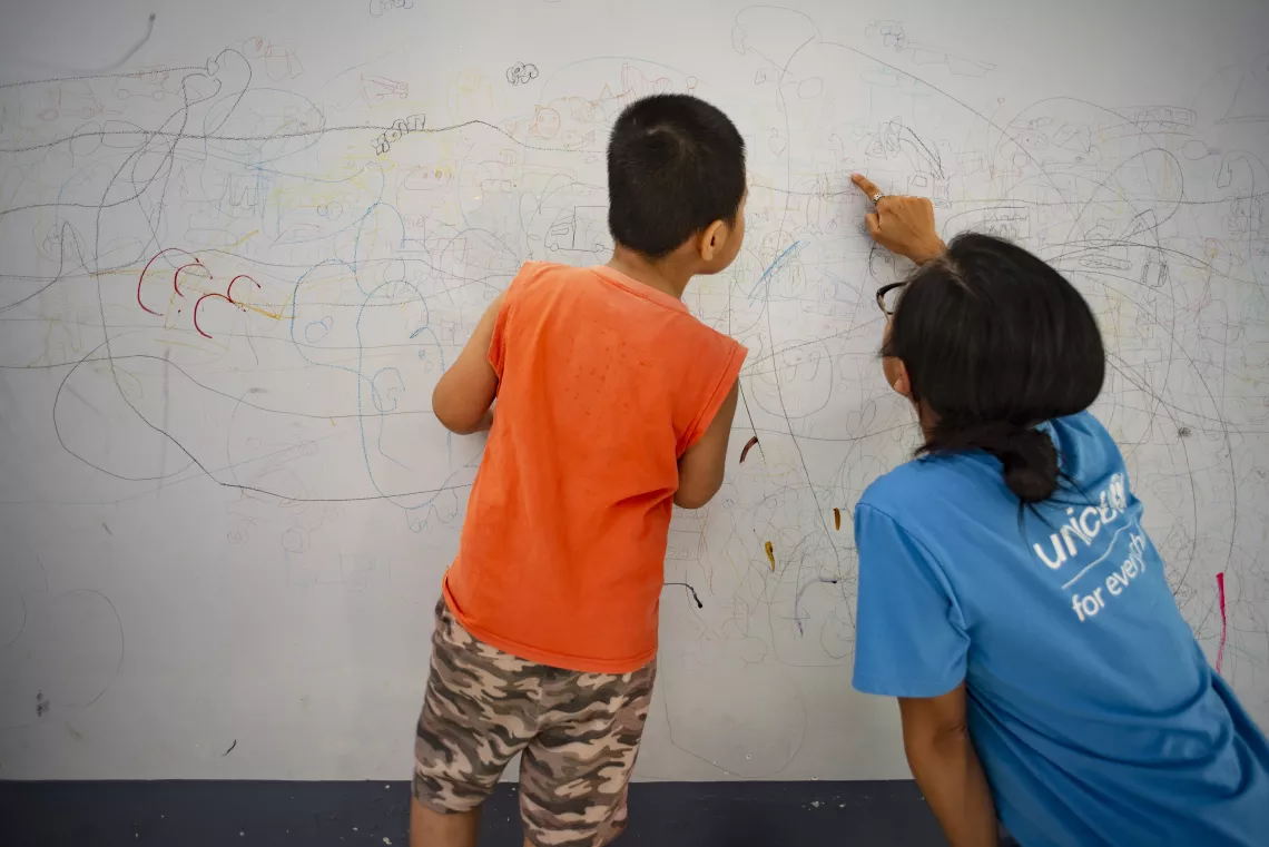 Nhan shows off his drawings on the wall to a UNICEF staff. Nhan learns to express his emotions and thoughts through drawing and coloring. 