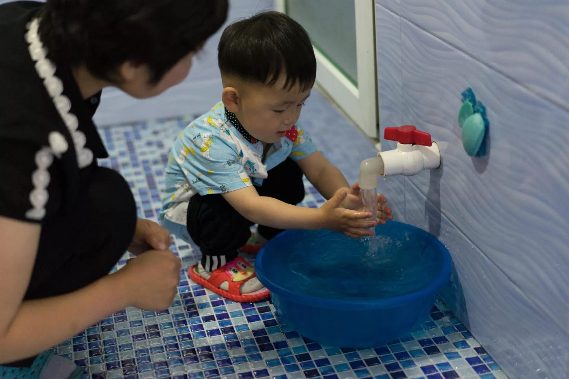 Two year old Jang Hun, with his mother Pae Hye Sim, washes his hands using a newly installed 24 hour gravity fed system in their home in jongju City, DPR Korea. 