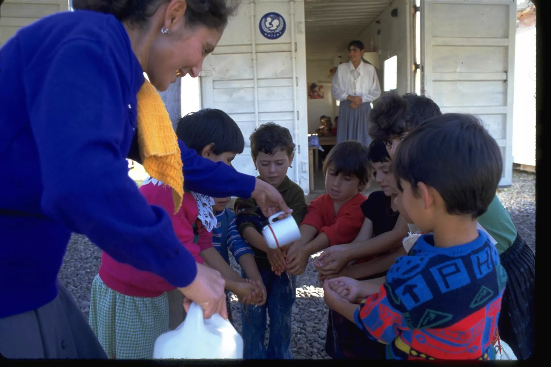 A woman teacher pours water over the hands of a group of children.