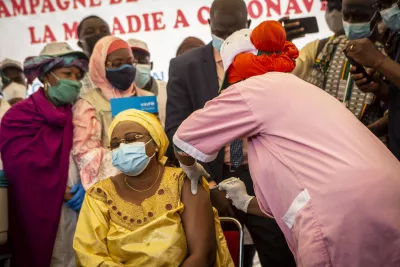 Woman wearing a yellow traditional outfit, sitting down as she gets vaccinated against COVID-19