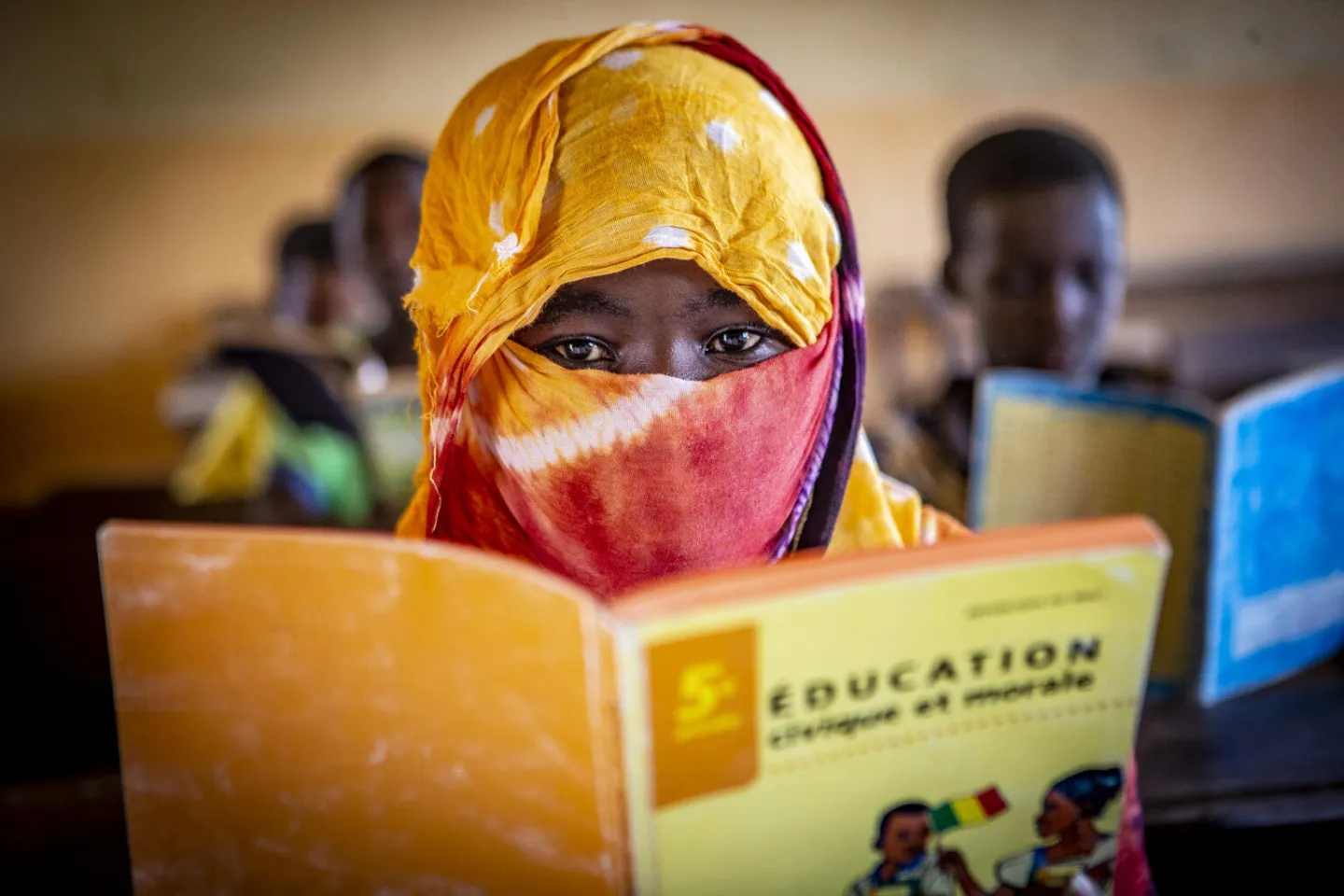 Portrait of a young girl wearing a yellow headscarf, holding a book at school