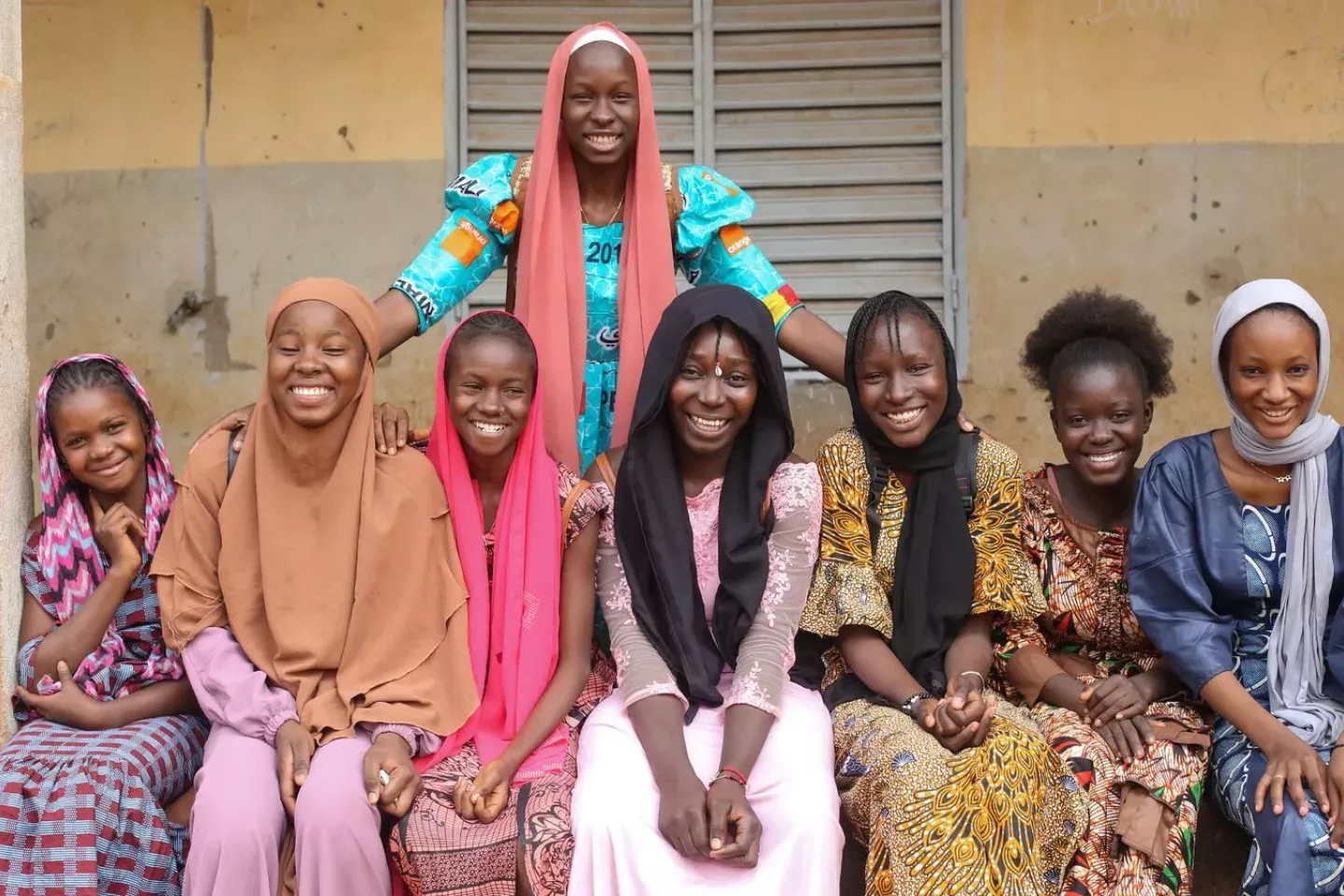 Eight adolescent girls wearing long traditional dresses and smiling outside