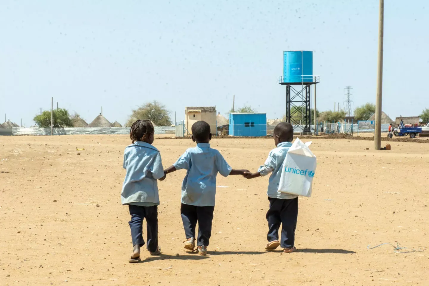 Three children walking away dress in school uniforms, outside in a sandy area