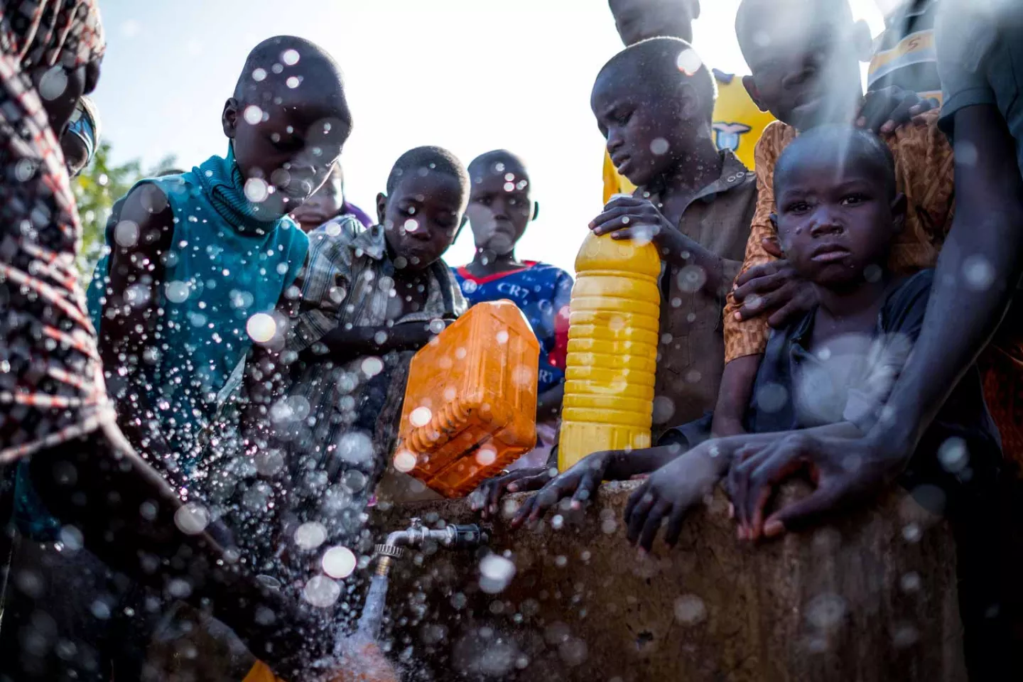 Water splashes as children fill jerrycans at an outdoor tap