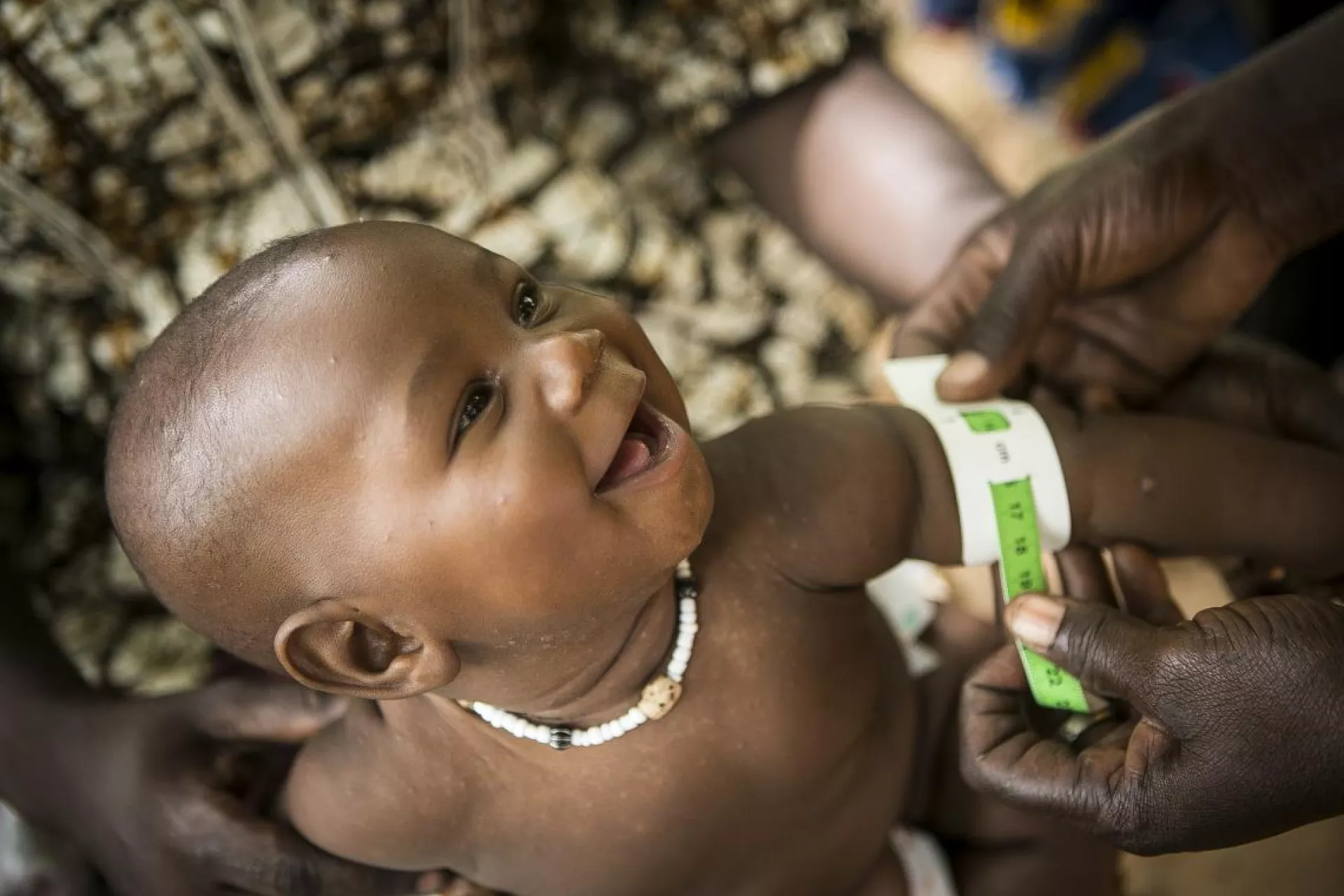A baby smiling as he is getting his mid-upper arm circumference measured
