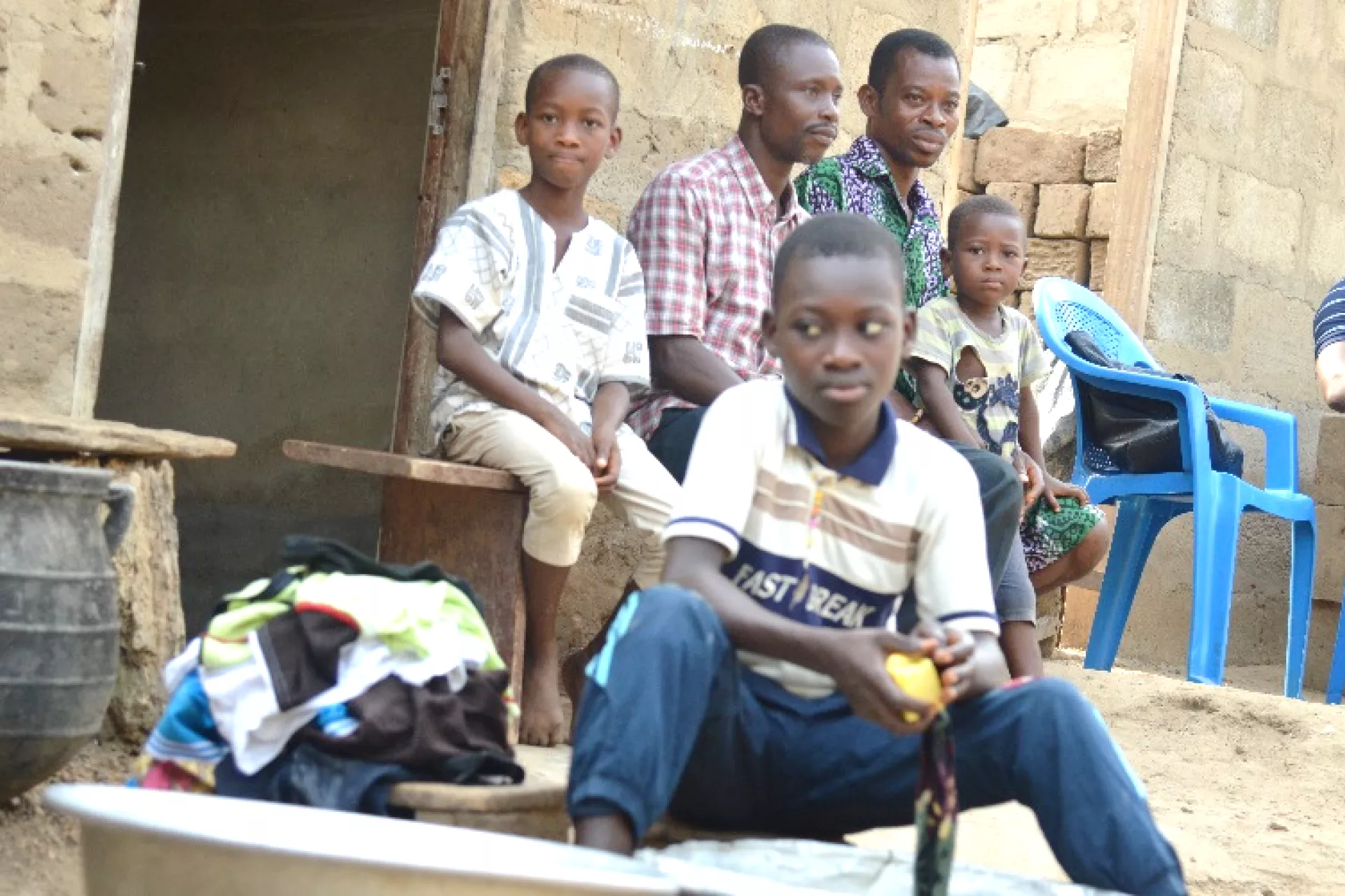 A young boy sitting doing laundry, with his father, teacher and siblings sitting in the background