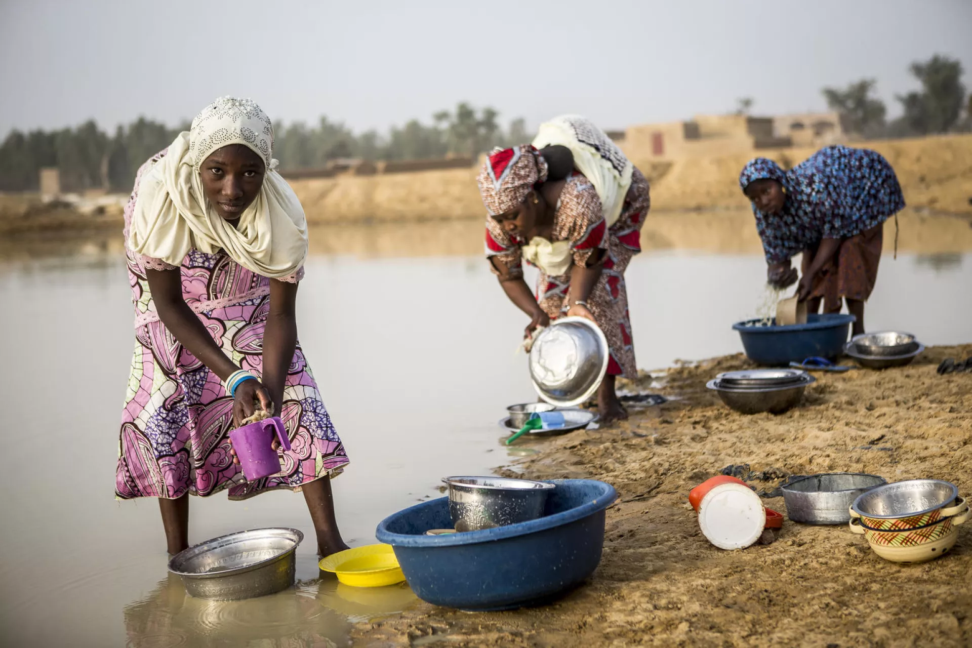 Three young girls washing dishes near a lake