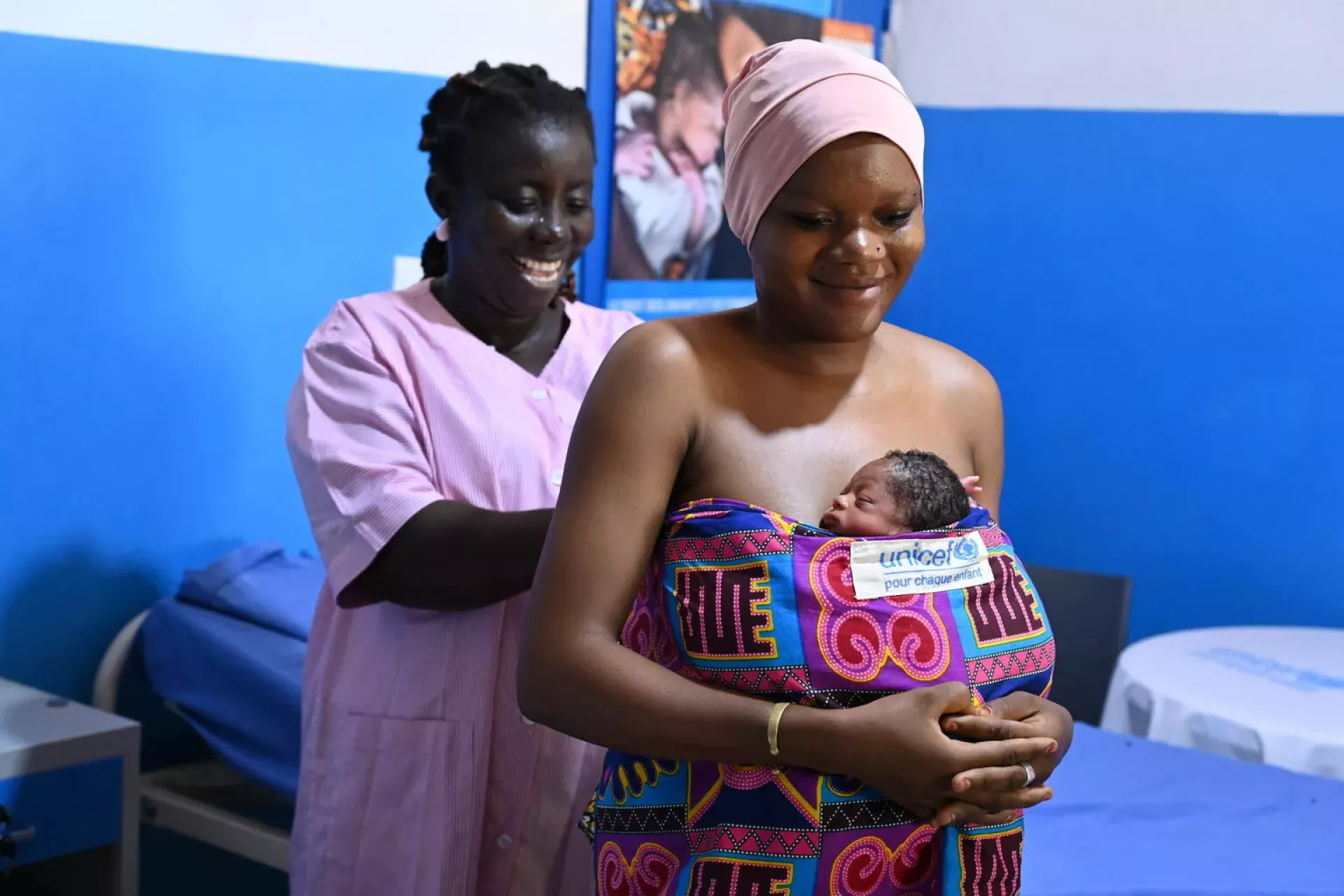 A midwife smiling as she helps a mother wrap her newborn on her chest