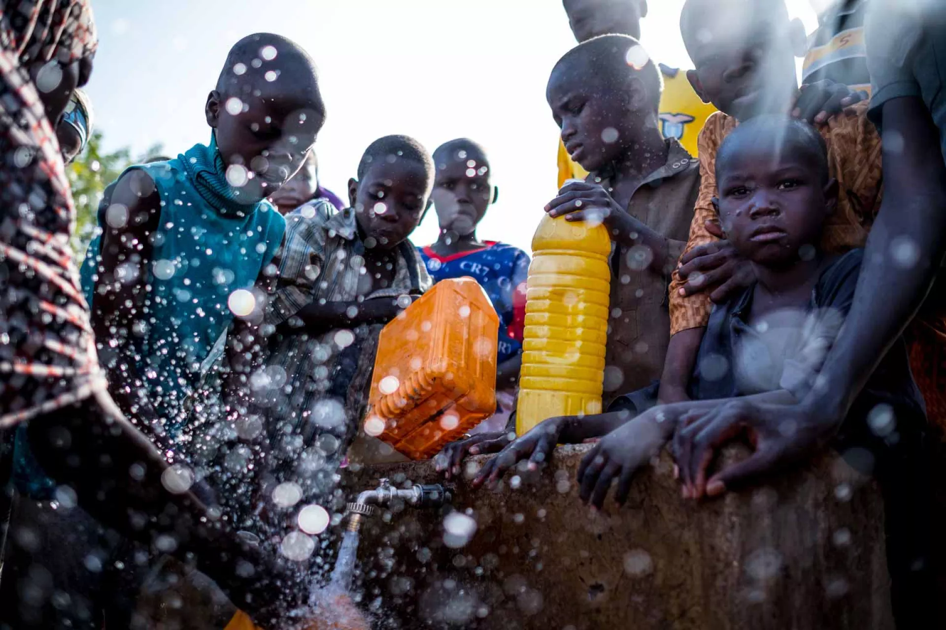 Water splashes as children fill jerrycans at an outdoor tap