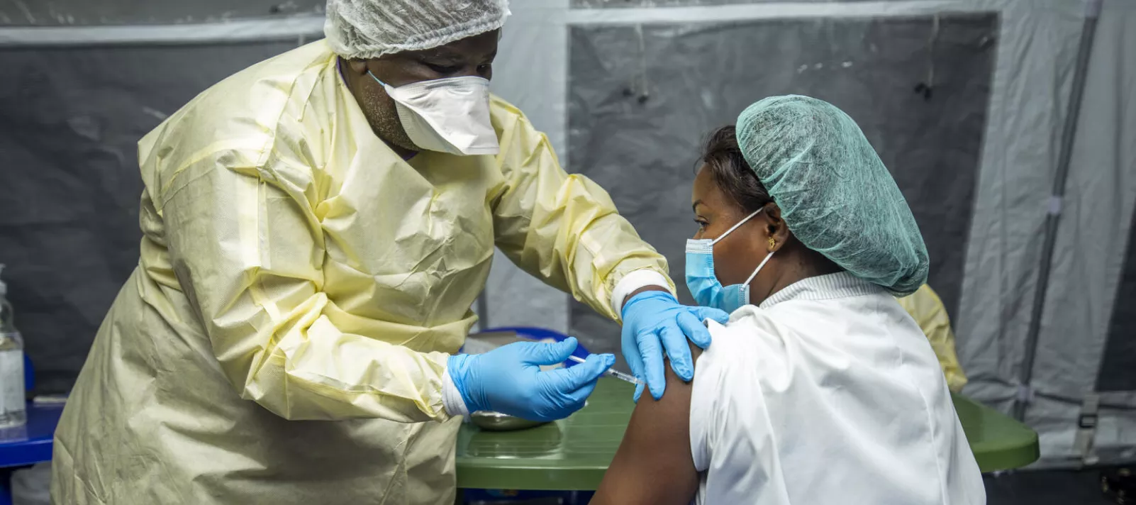 A nurse wearing protective personal equipment vaccinating another nurse