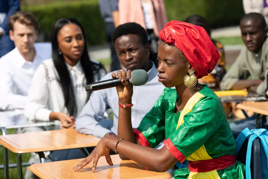 A young woman wearing traditional attire speaking into a mic while sitting at a desk