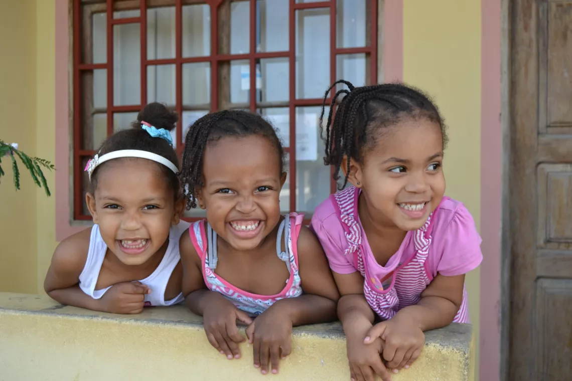 Three girls lean out of a window smiling