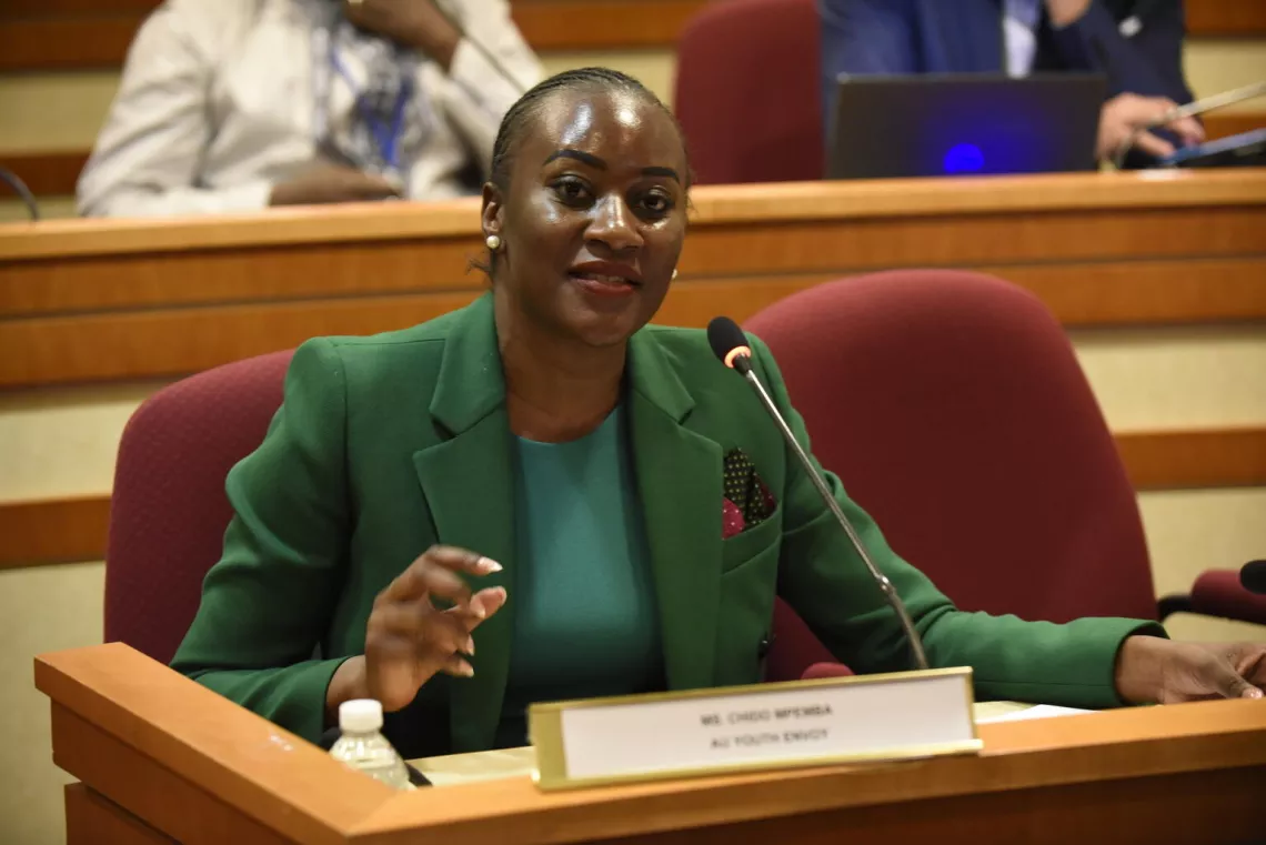 A young woman sitting in a conference room, delivering a speech