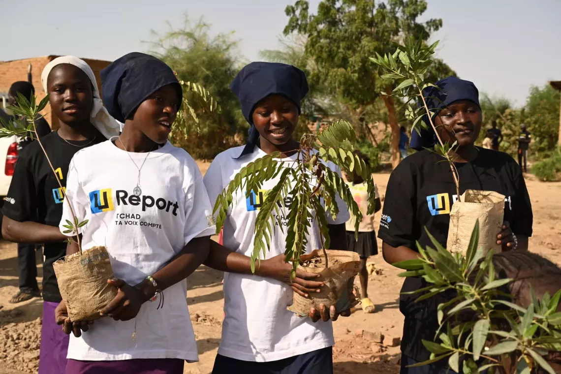 Four adolescent girls who are U-Reporters carrying plants