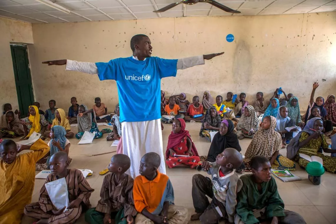 On 26 May, (standing), a teacher with his arms outstretched leads children in an activity at an informal learning centre in a UNICEF-supported safe space in the Dalori camp for internally displaced people, in the north-eastern city of Maiduguri in Borno State. 