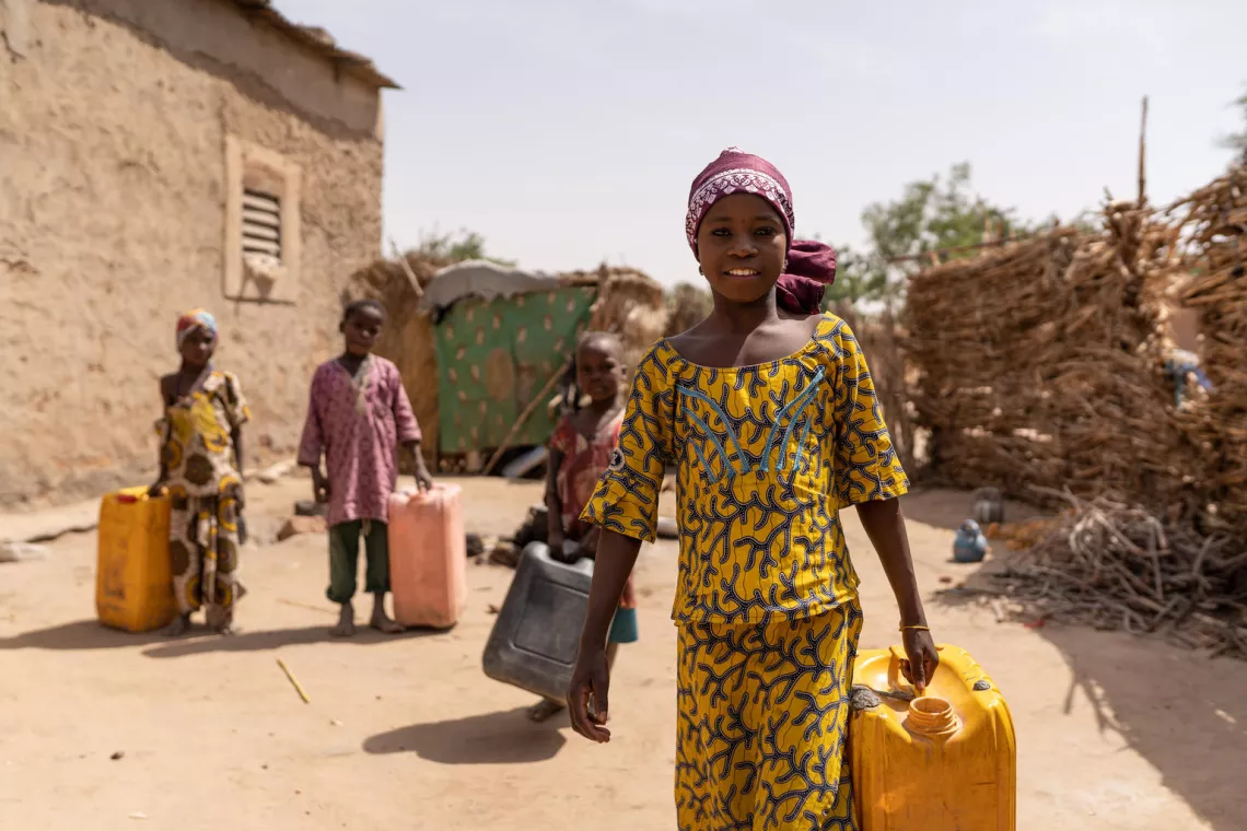 Une jeune fille avec d'autres enfants derri&egrave;re elle, transportant de l'eau