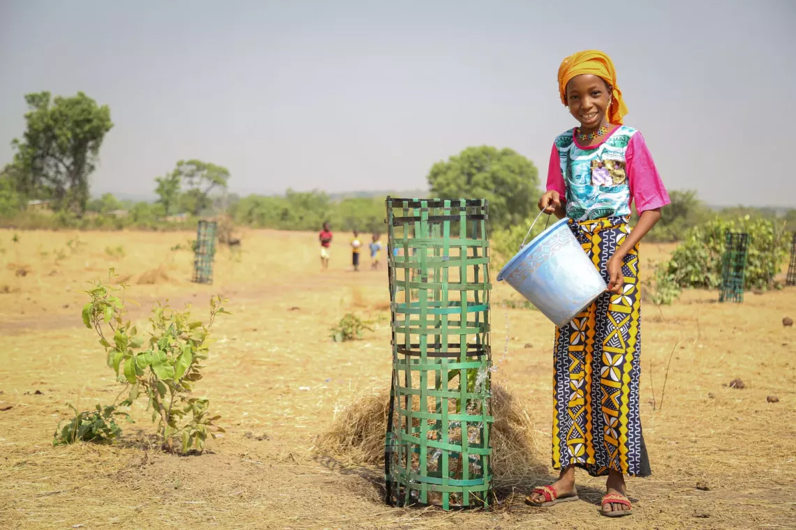 A girl standing outside watering a plant