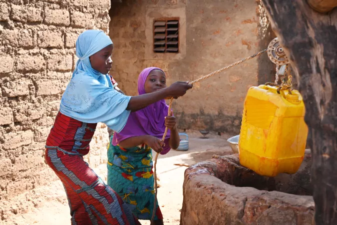 Two young girls fetch water from a well