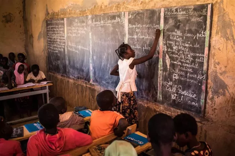 Une &eacute;l&egrave;ve &eacute;crit au tableau noir devant ses camarades dans une classe en Afrique.