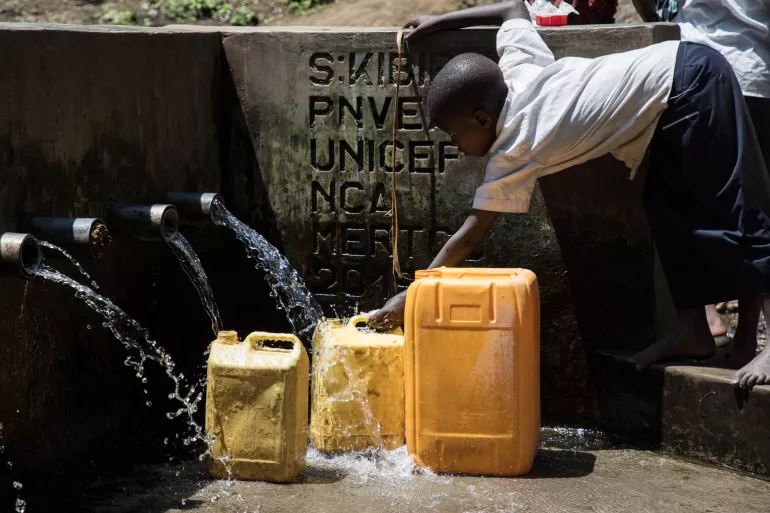 A child leans over to fillsup water cans through water taps