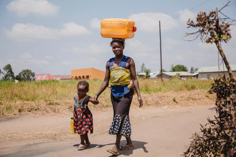 A mother carrying a water can on her head while holding her daughter's hand