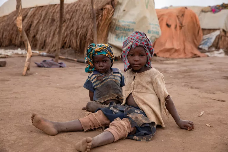 Two boys sitting on the ground outside in the camp for internally displaced persons