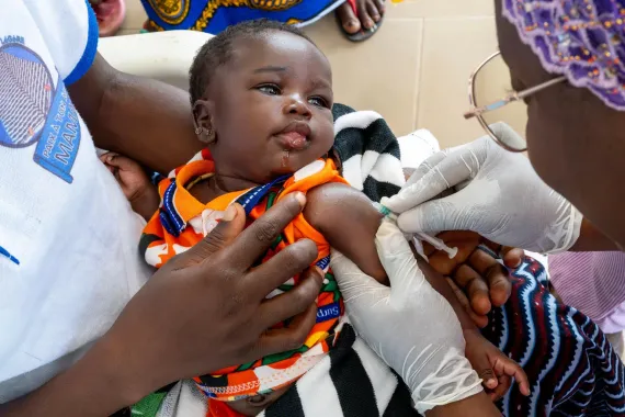 A baby held by mom, receives vaccine. 