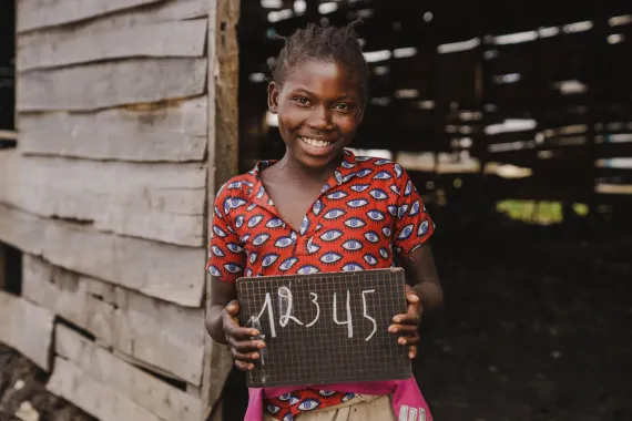 A student is holding a chalkboard in front of her class in the DRC 