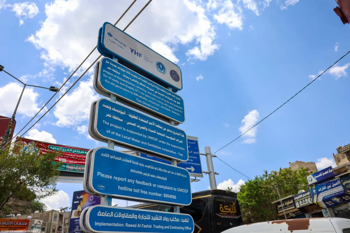 An outdoor project sign displaying information in Arabic and English about a UNICEF-supported local water and sanitation rehabilitation project in Taiz Governorate