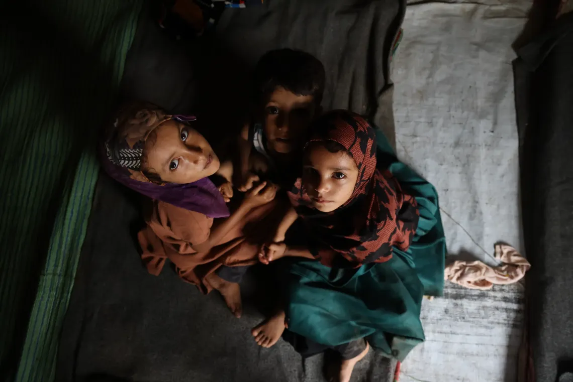Three siblings sitting on the ground looking at the carema