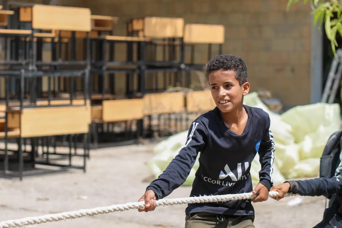 The boy holds a thick white rope, engaging in a game of tug-of-war alongside another participant partially visible on the right.