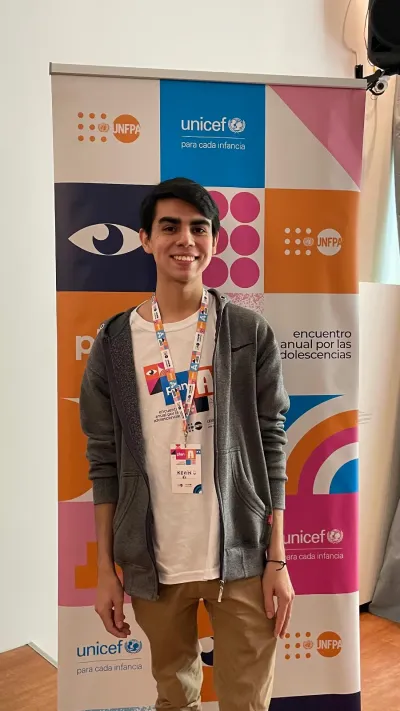 A photo of a young man smiling next to a UNICEF/UNFPA banner