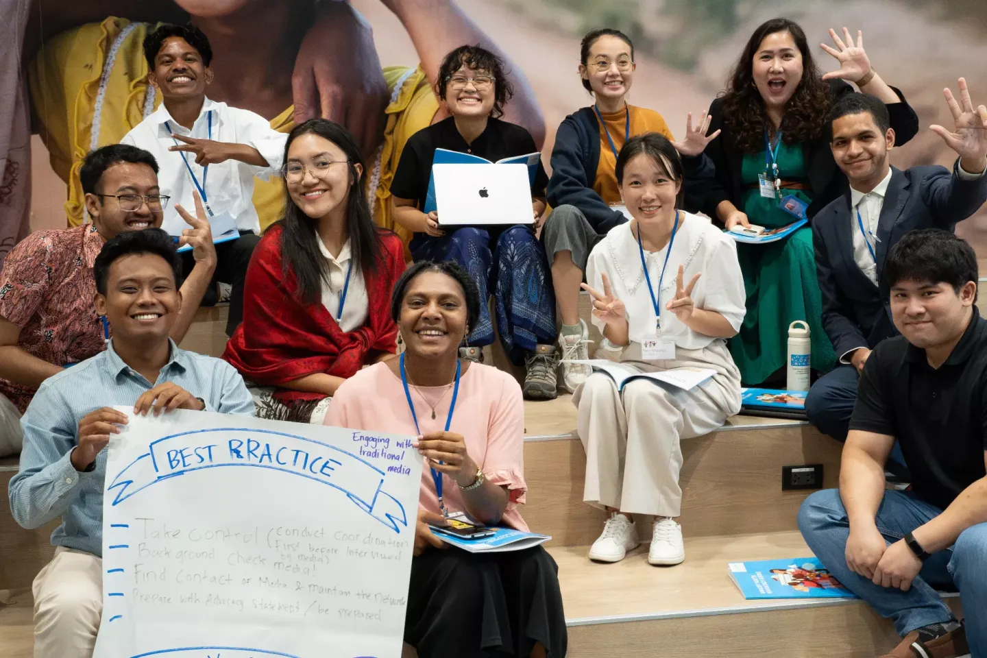 A photograph of a group of young people from the East Asia and Pacific region sitting together and smiling while working