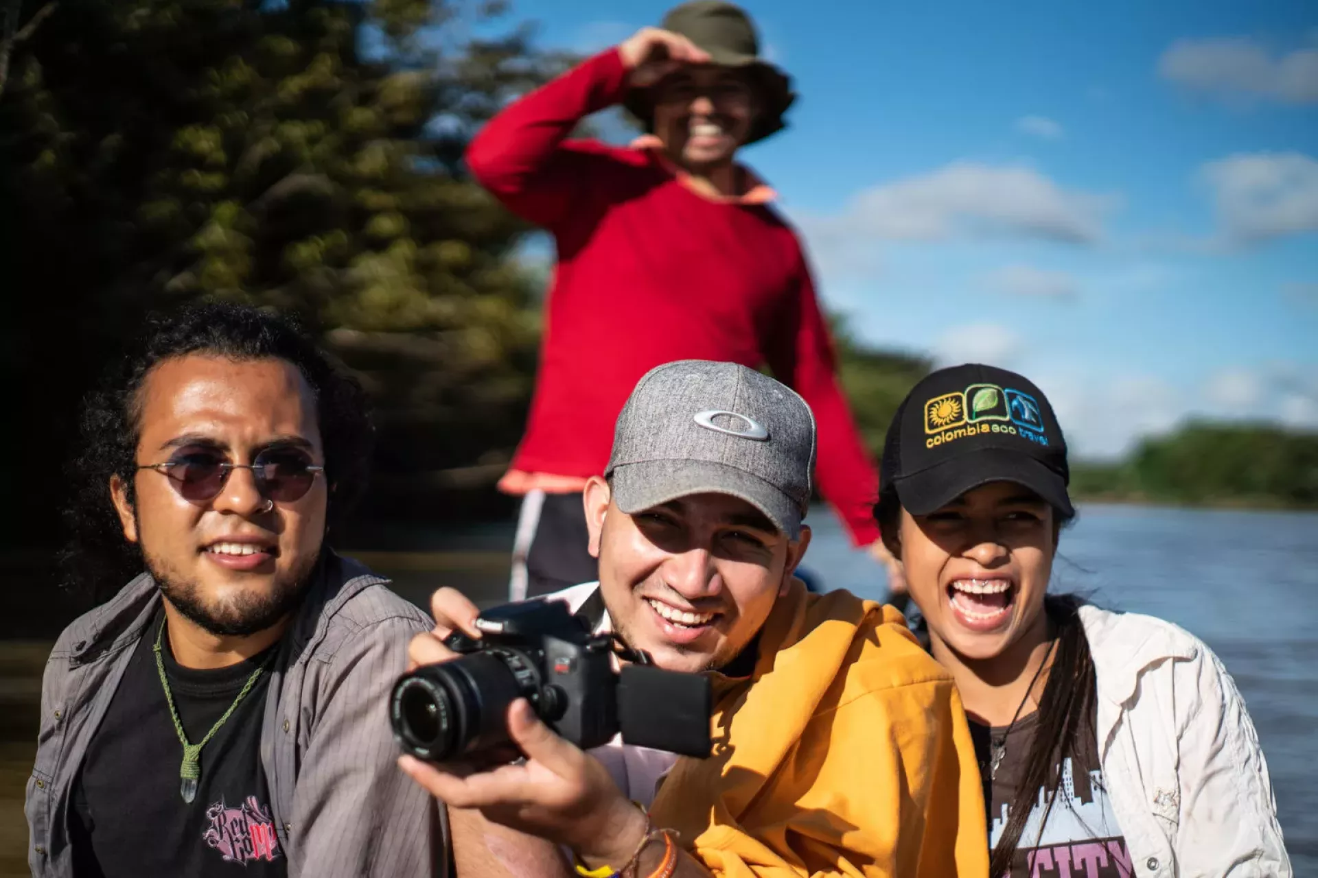 A photograph of three people on a canoe, smiling. One person is holding a camera.